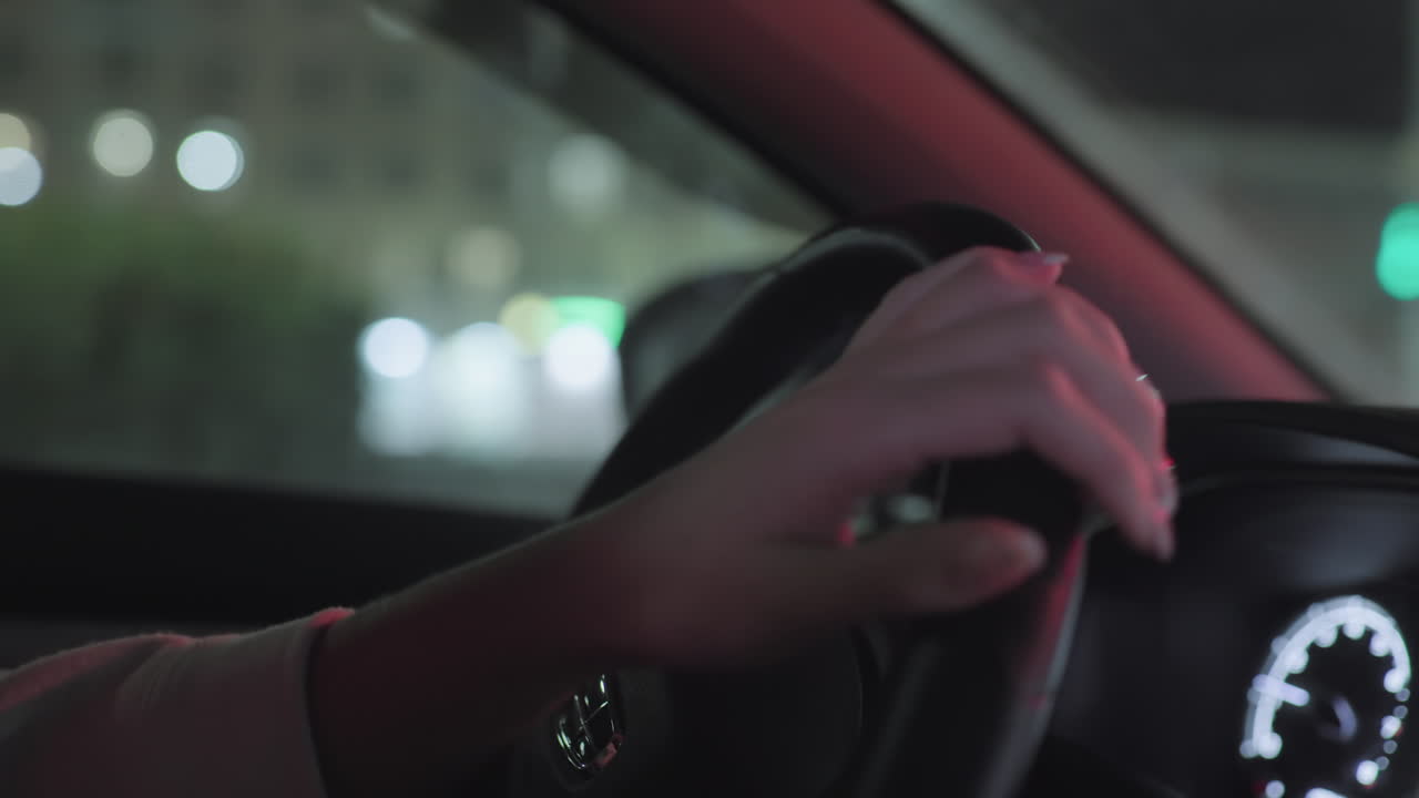 Close up of driver hand gripping steering wheel while driving at night, dashboard softly glowing with illuminated meters, exterior street lights casting gentle reflections through side window