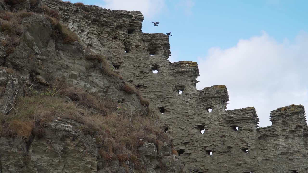Close up view of one of the Tintagel Castle is a medieval fortification located on the peninsula of Tintagel, Cornwall . Medieval fortification ruins with some crows landing on the edges of the wall