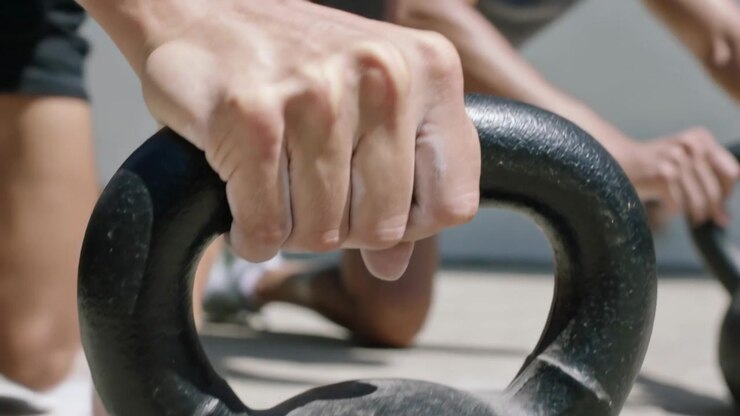 Clapping chalk dust, man in tank prepping grip, reaching, grasping kettlebell on sunlit patio