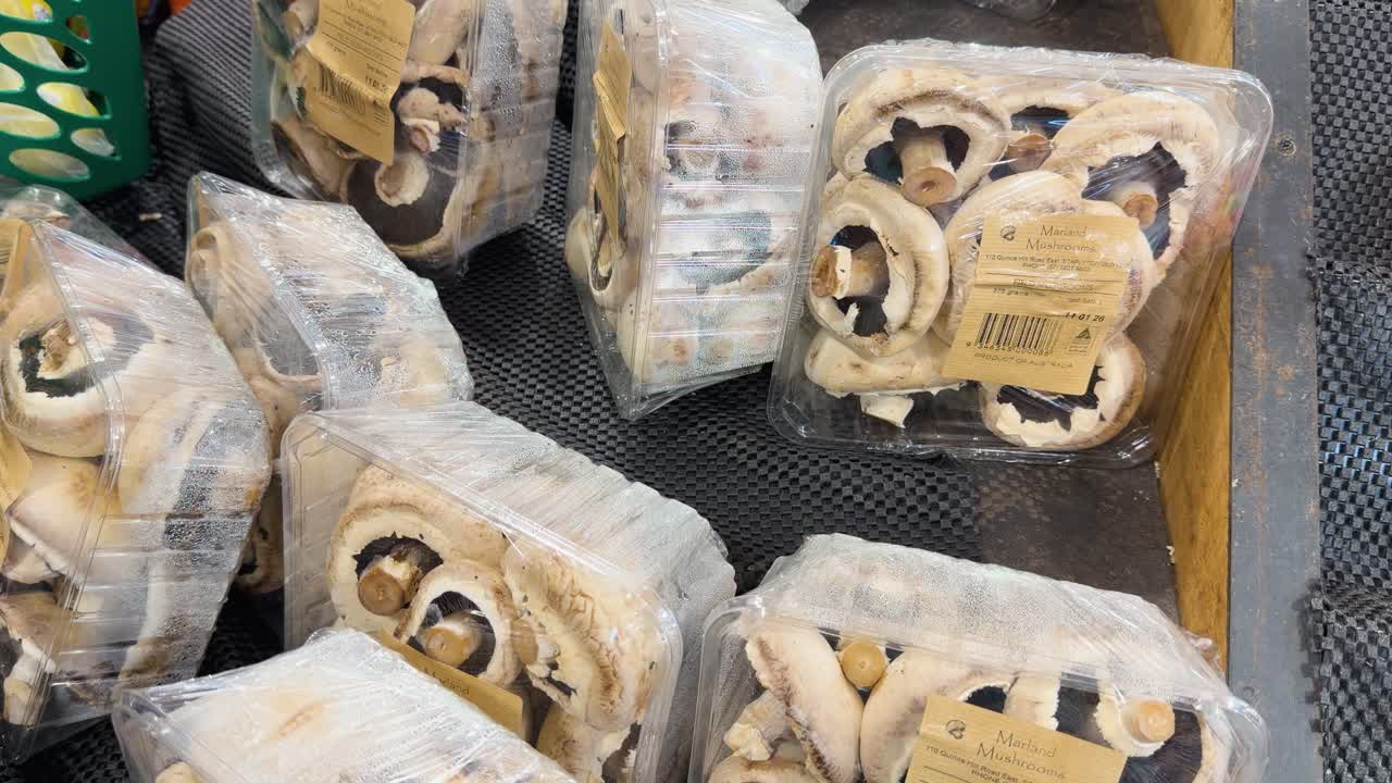 A close-up shot shows a hand picking up a plastic container of fresh mushrooms