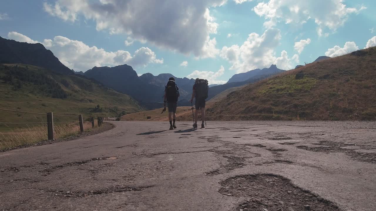 vista trasera de dos excursionistas con mochila grande caminando hacia el pico de la montaña en la soleada tarde puesta de sol en verano