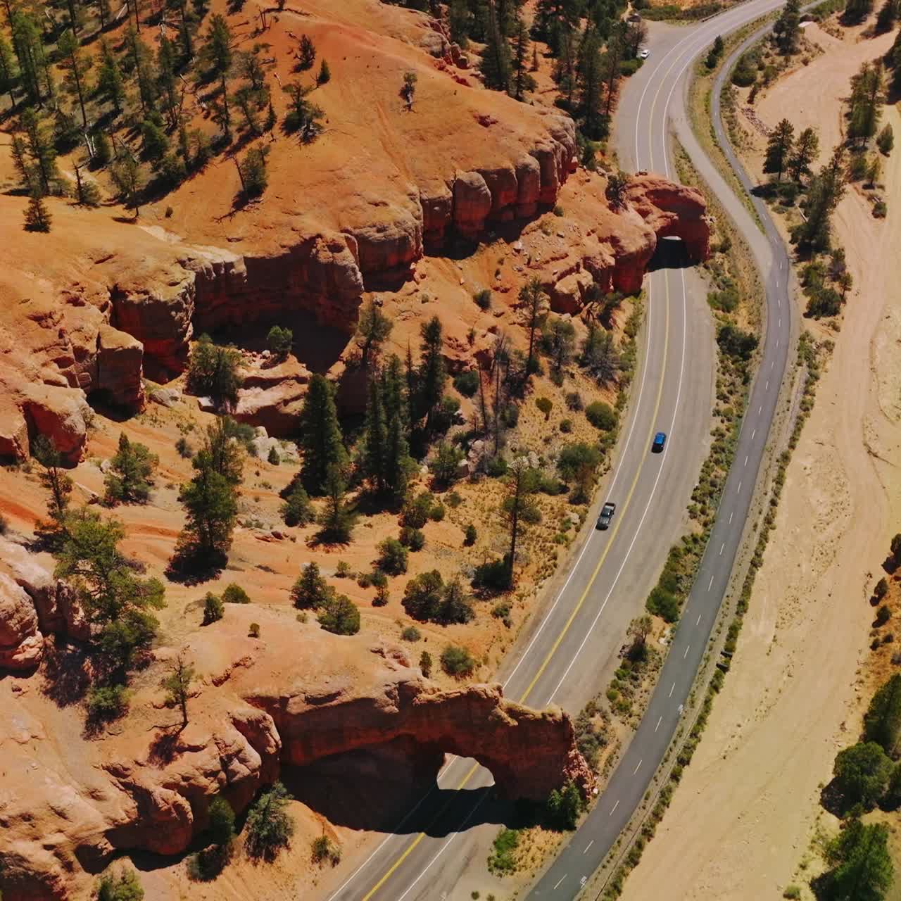 Cars going under the rock arches on the highway in National Park. Sunny daytime footage over the Arches canyons, Utah, USA