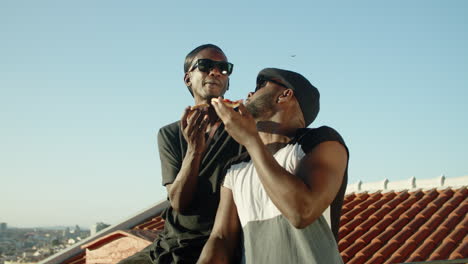 satisfied gay couple sitting on rooftop and eating pizza