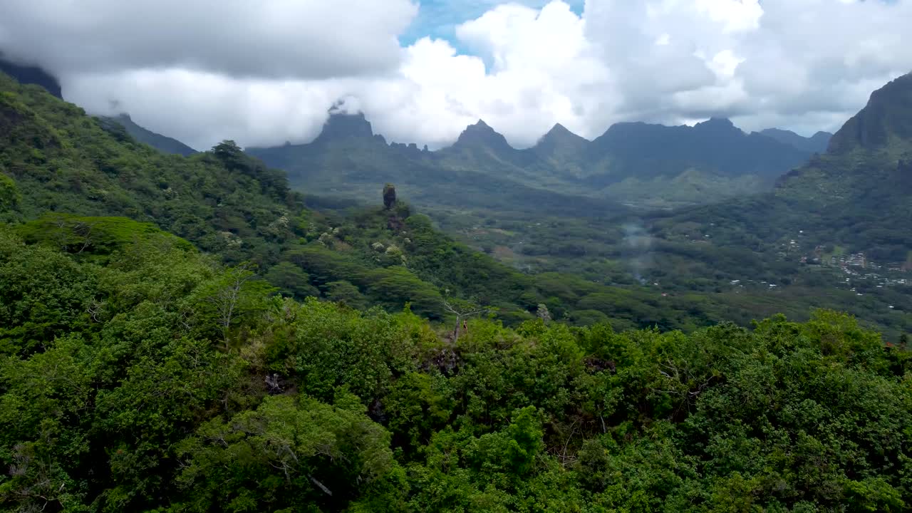 Drone view of a caucasian woman walking through nature on a mountain ridge in a jungle surrounded by mountains in Moorea, French Polynesia.