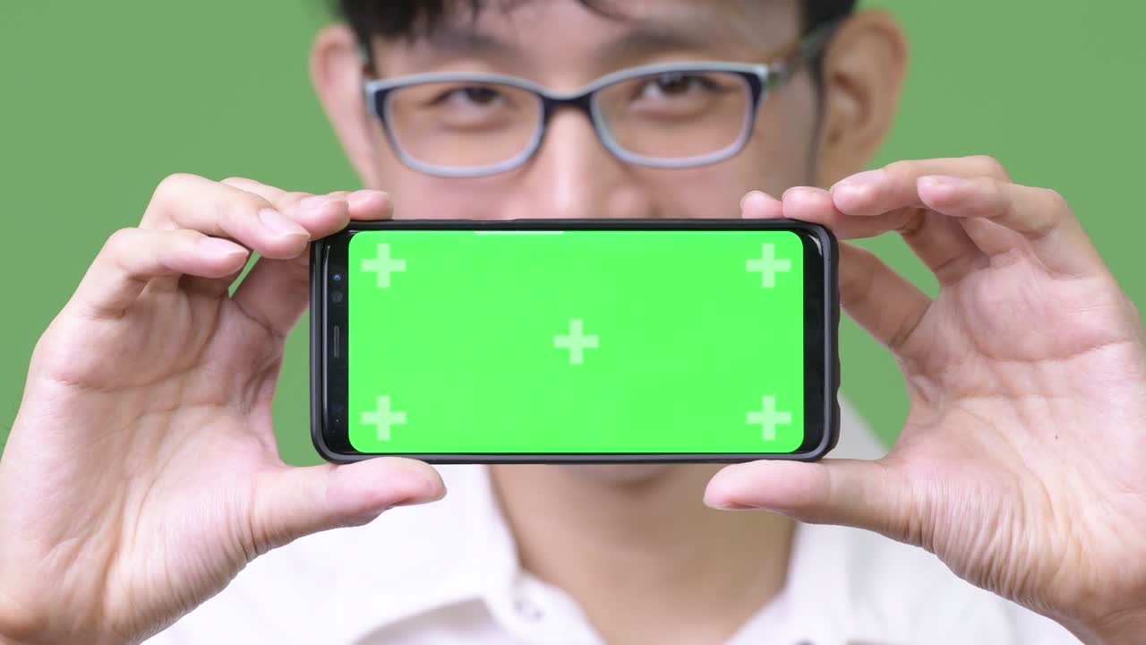 젊은 아시아 사업가 가 카메라 에 전화 를 보여주고 있다