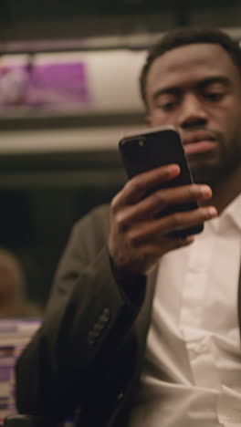 vertical video of young businessman in suit commuting to work sitting in london underground tube train wearing wireless earbuds to stream from mobile phone shot in real time 1