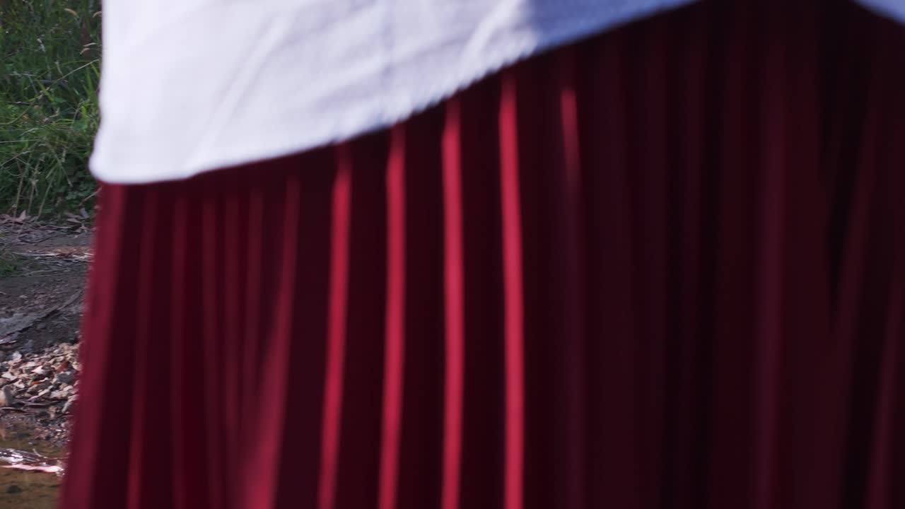 Primo piano focalizzato di tessuto rosso testurizzato con luce naturale all'aperto, che mostra pieghe e ombre intricate. La scena cattura toni terrosi ed elementi naturali sullo sfondo.