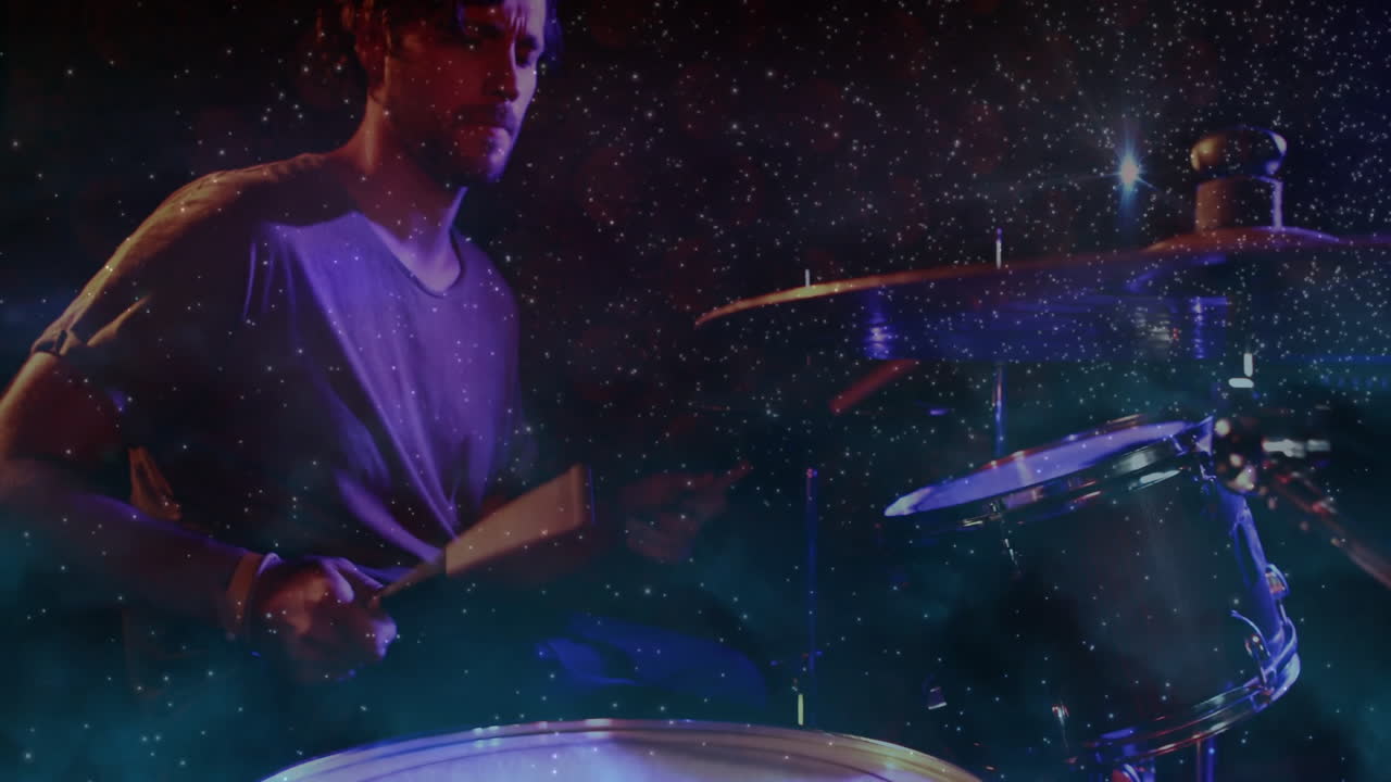 Male drummer performing drums on stage under blue-purple spotlights with cosmic particle overlays