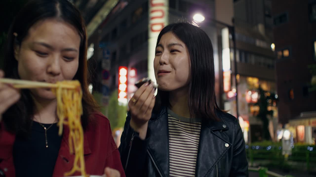 Two women enjoying street food in a Japanese city at night