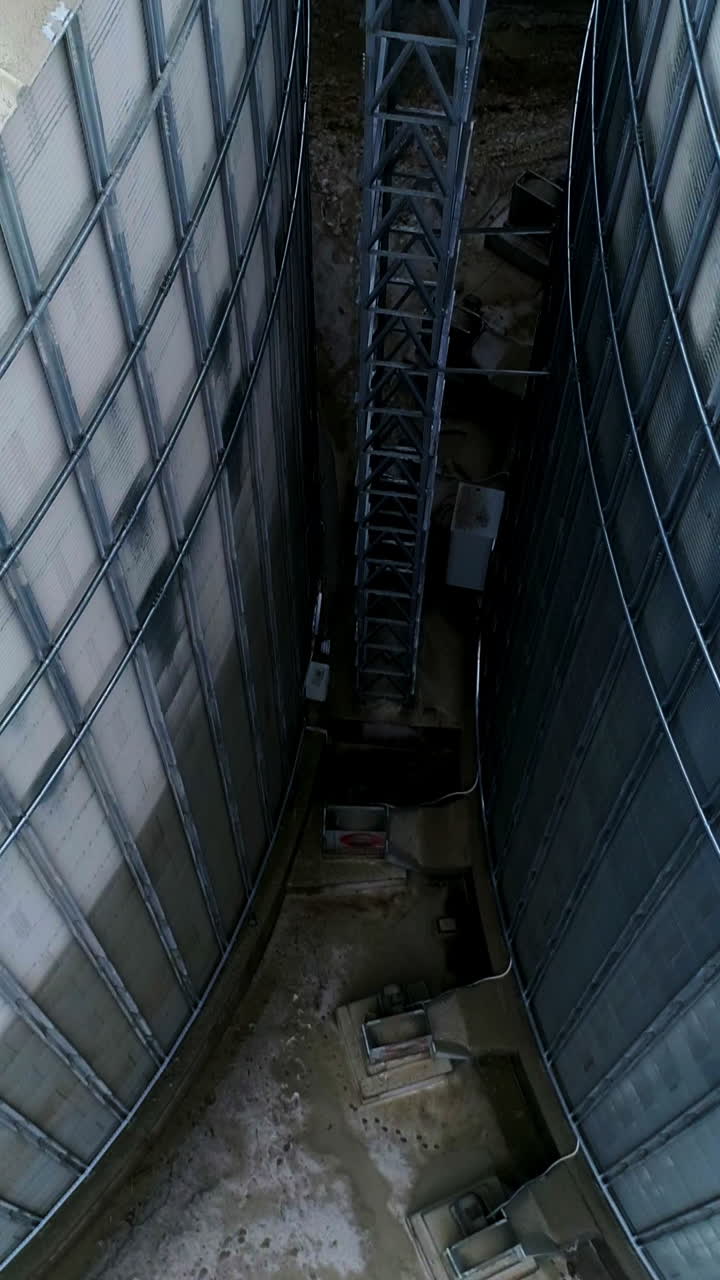 Going down among two huge metal granary tanks. Exterior footage of the modern silo complex on winter day. Vertical video