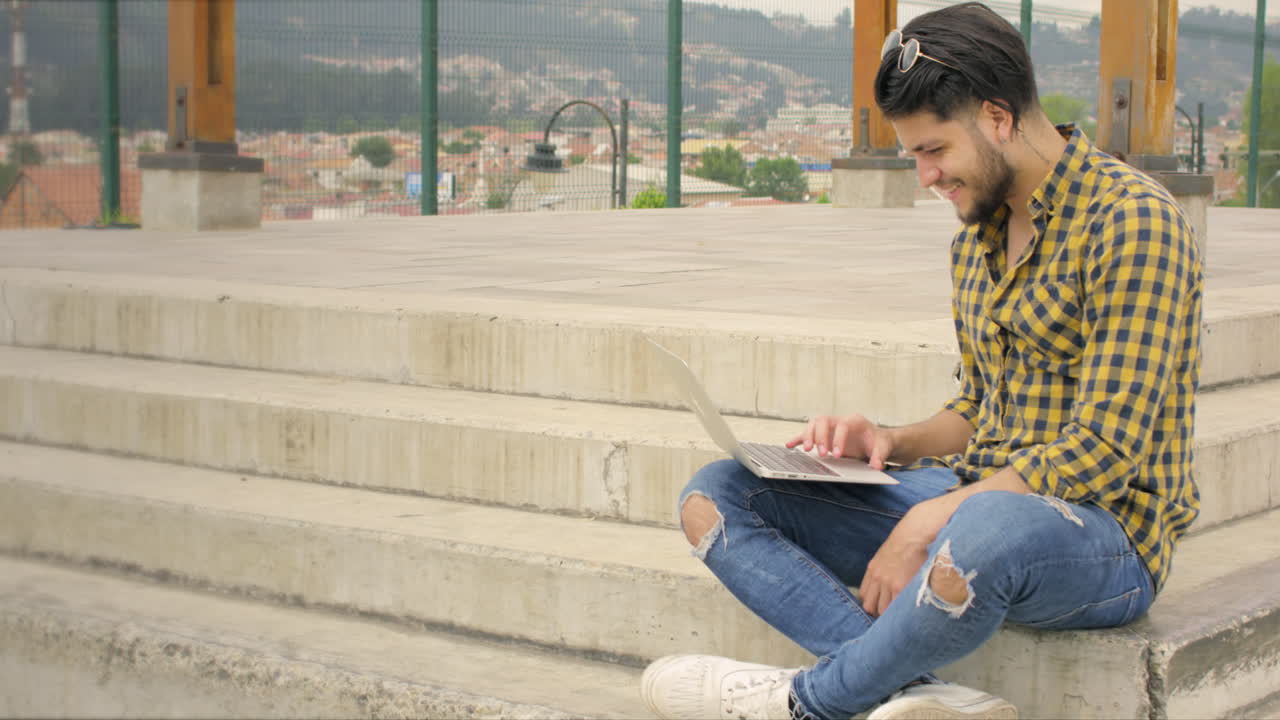 hombre guapo sentado en las escaleras usando una computadora portátil al aire libre