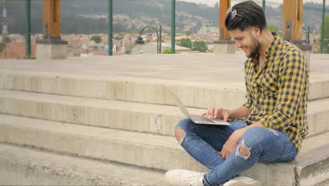 Hombre-Guapo-Sentado-En-Las-Escaleras-Usando-Una-Computadora-Portátil-Al-Aire-Libre