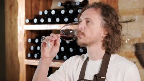 authentic shot of successful male sommelier is tasting a flavor and checking white wine quality poured in transparent glass in a wine cellar.