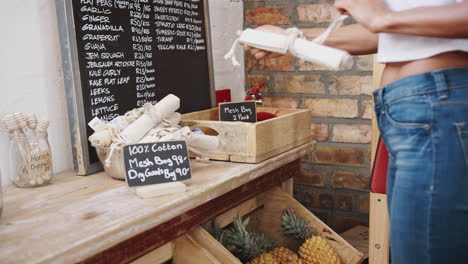 Close-Up-Of-Woman-Putting-Pineapple-Into-Reusable-Cotton-Bag-In-Plastic-Free-Grocery-Store