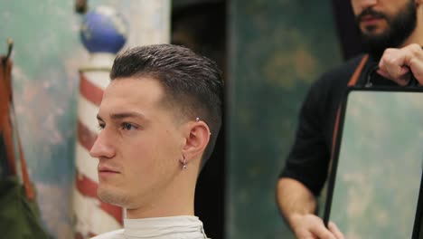 Professional-hairdresser-shows-the-back-view-of-the-haircut-using-mirror-to-handsome-satisfied-male-client-in-a-professional