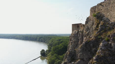 rotating side angle drone shot of the hrad devin castle with birds flying around the cliffs