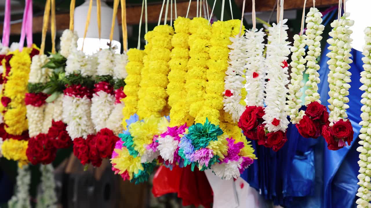 Rows of vibrant flower garlands hang in a bustling Singapore market, captured with smooth camera panning and bright, natural lighting