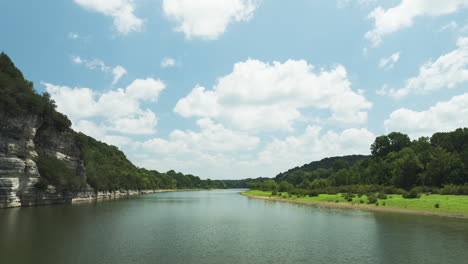 river flowing between green hills under a bright blue sky with scattered white clouds