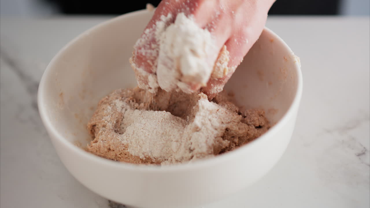 Close up of a woman's hands kneading dough in a white bowl