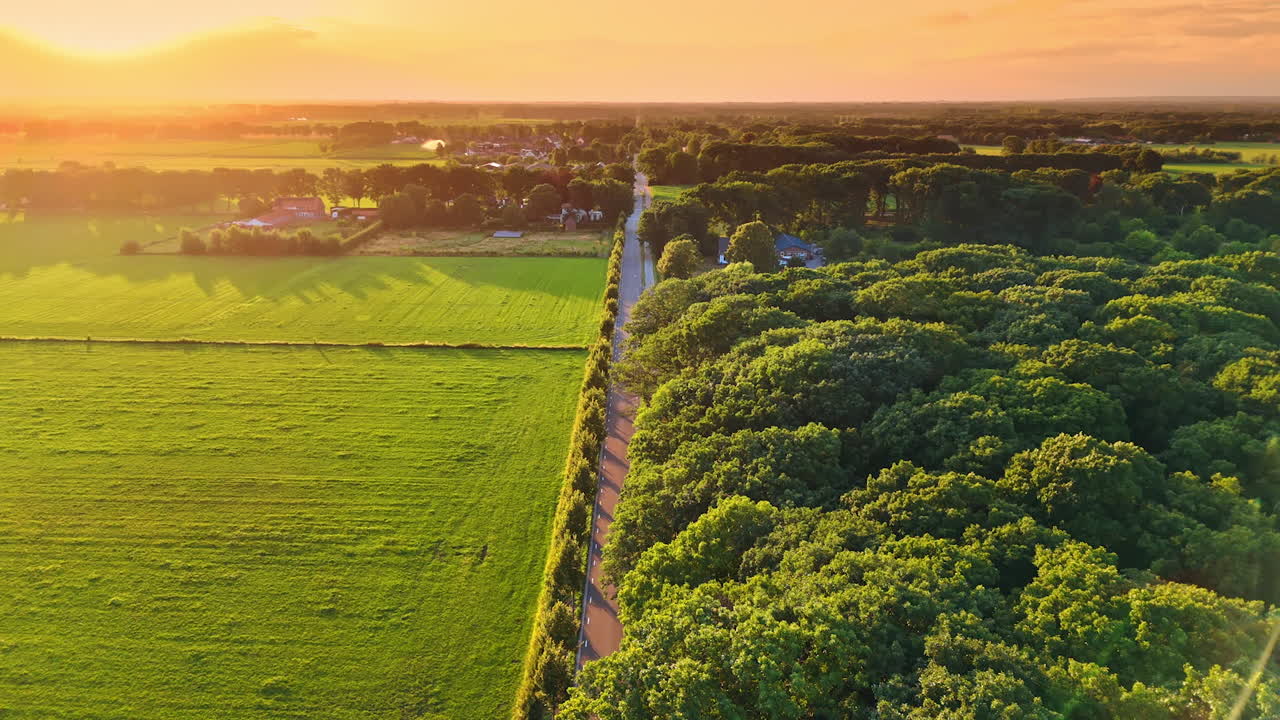 Sunset over green countryside. Golden sunlight casts a warm glow over rolling green fields and a winding road, showcasing serene evening beauty