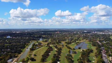 una vista aérea panorámica de un campo de golf ubicado en un suburbio, en un día parcialmente nublado, a 60 fotogramas
