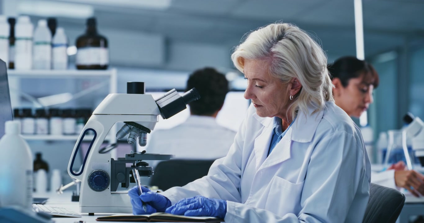 Senior Scientist Using Microscope and Taking Notes in Laboratory