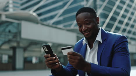 african american man using phone and credit card for online payment