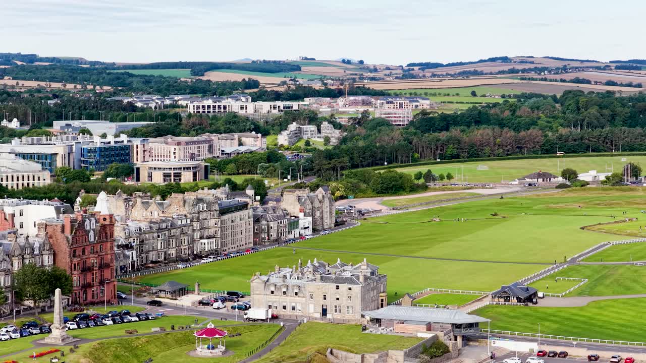 Drone pans across classic stone clubhouse, green fairways, and historic buildings under daylight skies