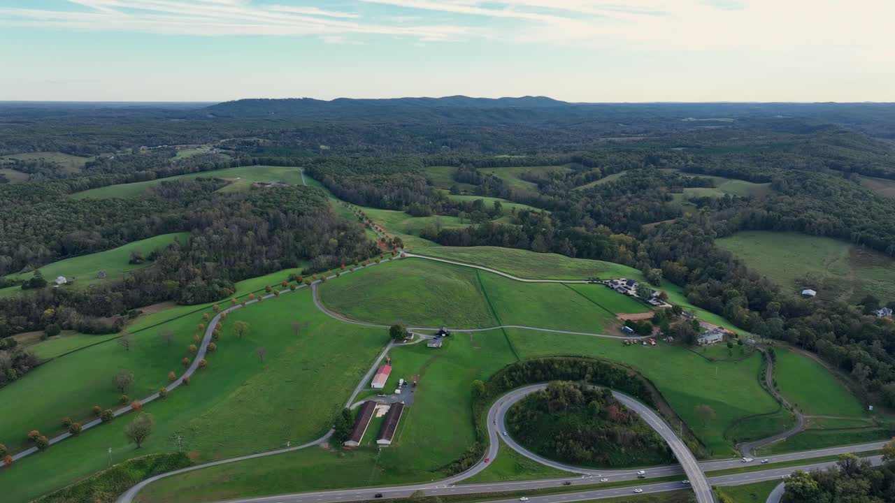 Traffic on highway between green mountains with forest trees in autumn. Hilly Avenue with colorful trees in fall. Aerial wide shot. Top down.