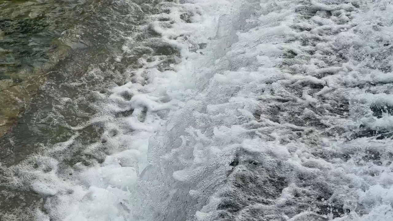 White frothy cascade flowing over rugged rocks, seen from above. The rushing current creates dramatic textures, energy, and a refreshing natural scene ideal for nature, travel, or relaxation themes.