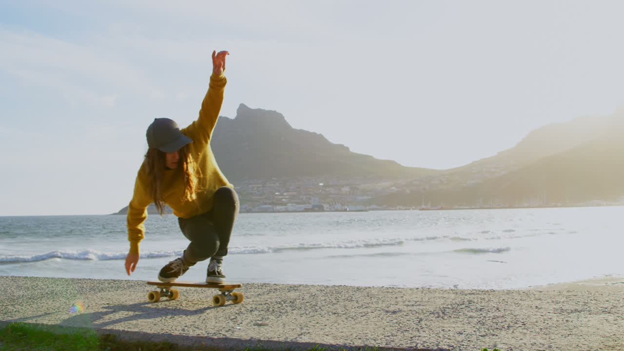 vista frontal de una joven mujer caucásica practicando un truco de skateboard en el pavimento de la playa 4k