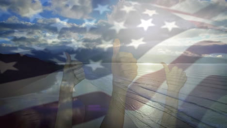 digital composition of waving us flag over hands showing thumbs up against sea waves