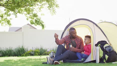 Happy-african-american-father-and-his-son-sitting-in-tent-in-garden