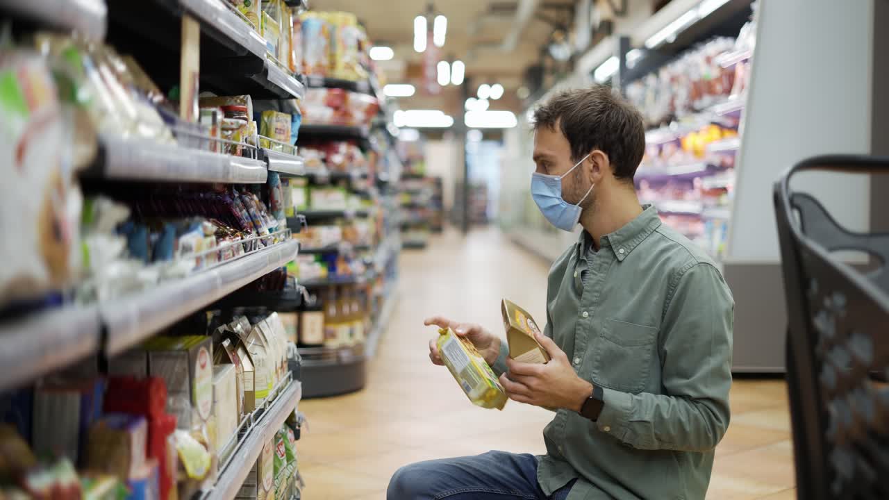 hombre con máscara toma comestibles del estante de alimentos. comprador eligiendo bienes en la tienda de comestibles