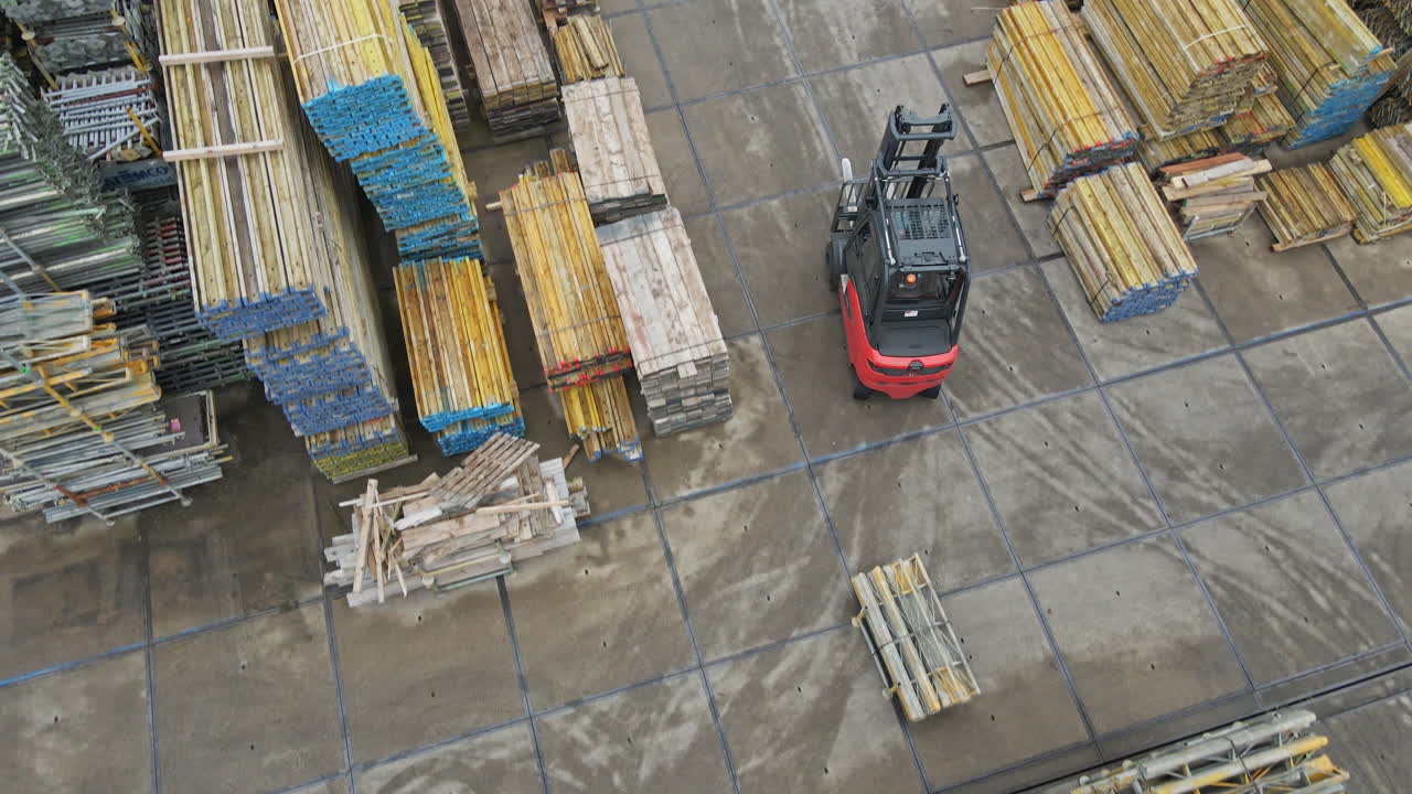 Aerial of a forklift truck driving over industrial storage yard filled with high stacks of construction materials