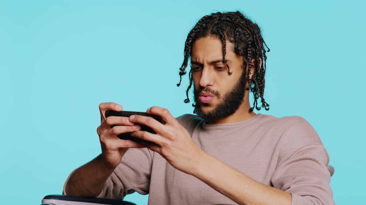 Man with disability in wheelchair playing videogames on cellphone, studio