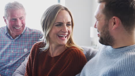 senior parents with adult offspring sitting on sofa at home talking and laughing