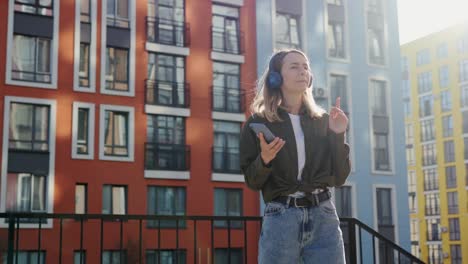 phone application girl listening to music in urban city background. young adult happy woman dancing in downtown very emotional. happy young woman in wireless headphones dancing singing outdoors.