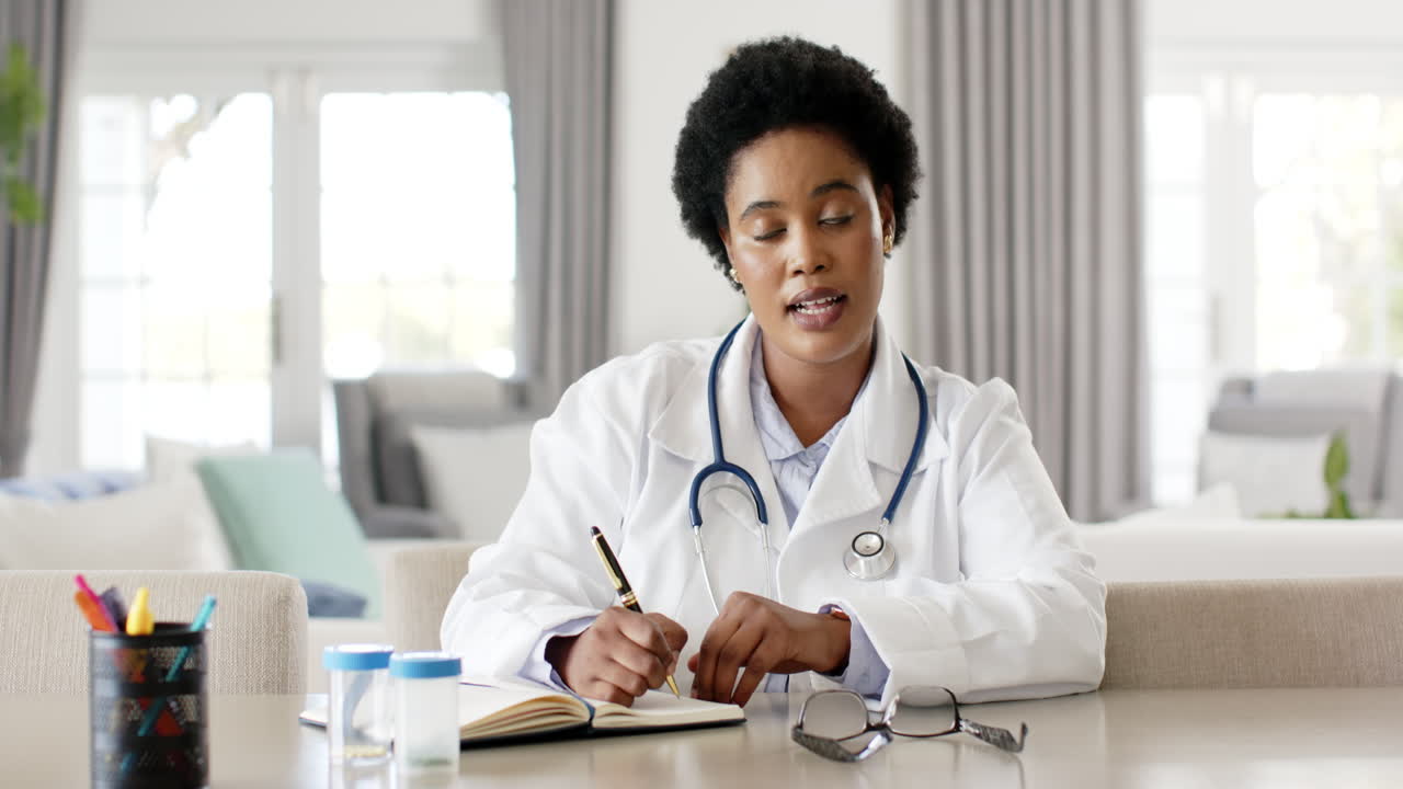 African American female doctor in a white lab coat is writing notes on video call consultation