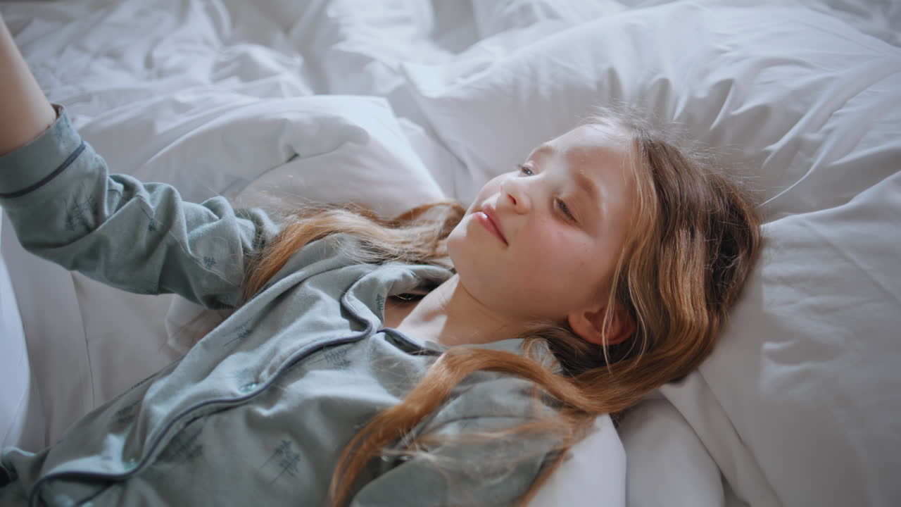 Pyjamas child lying sunlight bedroom alone closeup. Relaxed kid playing mirror