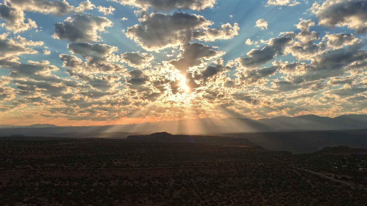 Timelapse in 4K con drone che sorvola un vasto paesaggio di mesa. Splendidi raggi di sole filtrano attraverso nuvole mattutine sparse, proiettando fasci di luce brillante e ombre in movimento sul terreno desertico accidentato.