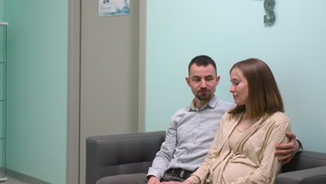 pregnant woman and her husband sitting on sofa waiting for gynecologist in medical consultation 1