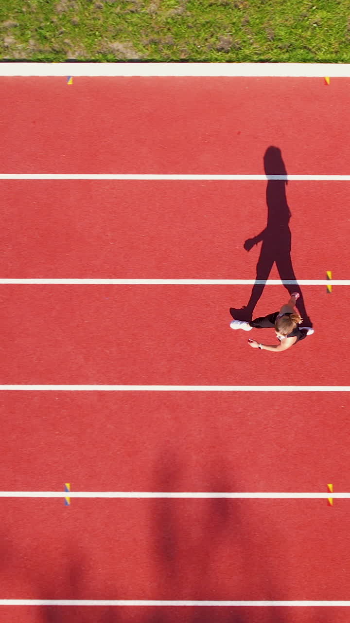 Ripresa verticale dall'alto di un'atleta che scatta su una pista da corsa rossa. Perfetto per contenuti su fitness, motivazione sportiva e stile di vita sano.