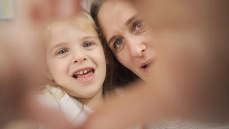 Mother-and-daughter-are-making-hearts-and-looking-at-camera.