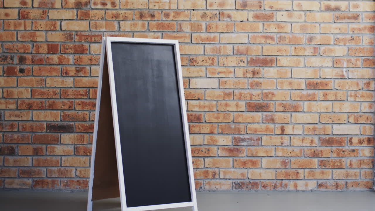 Video of blackboard sign on white stand with copy space on brick wall background