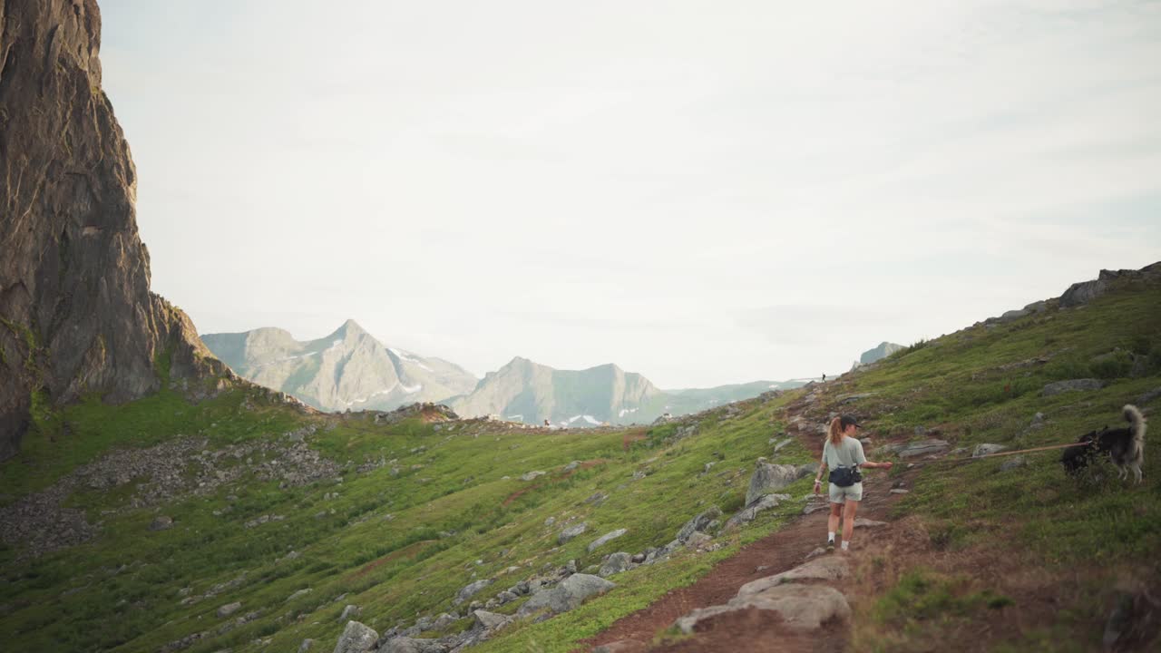 mujer caminando con un perro doméstico en el sendero hesten cerca de la montaña segla en noruega