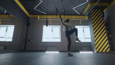 doing trx exercises. young athletic woman in sports clothing training legs with trx fitness straps in the gym. exercise where stabilizing muscles trained and the whole body is working truly functional