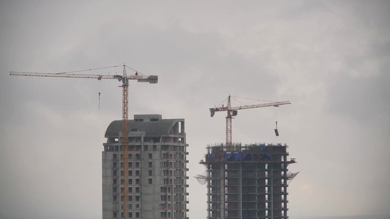 Grúas de Construcción Trabajando en Edificios de Gran Altura Bajo un Cielo Nublado
