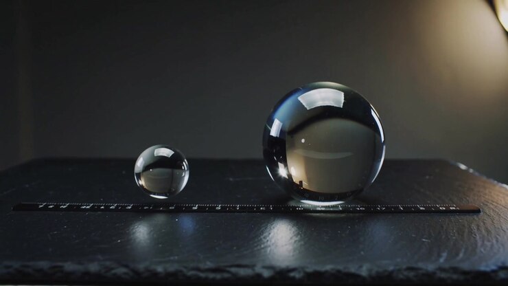 Pulling back camera on studio table revealing lamp shifting highlights on two glass orbs with ruler