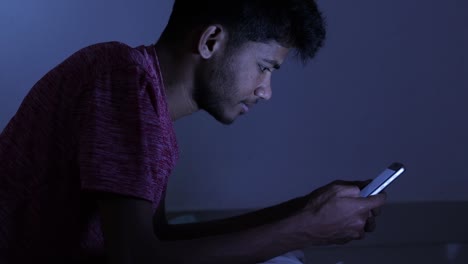 young indian teenager laying on the bed and using mobile while sleeping during the night on bed